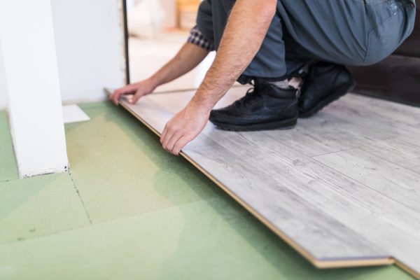 Worker installing wooden laminate flooring in living room