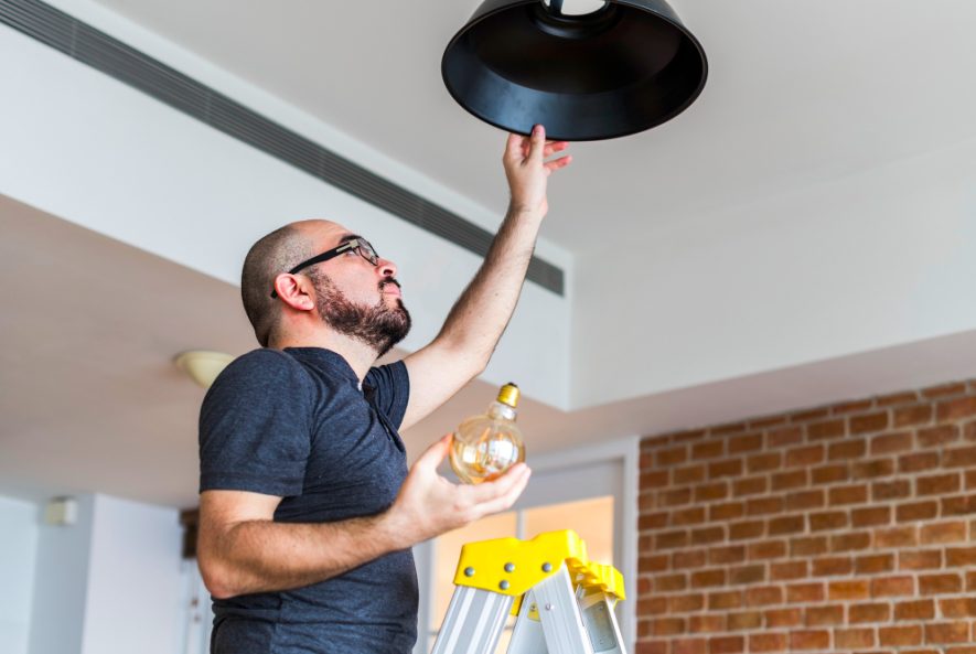 Electrician installing ceiling light fixture in modern home
